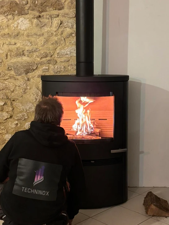 Intérieur chaleureux avec poêle à bois en fonctionnement, flammes visibles derrière la vitre