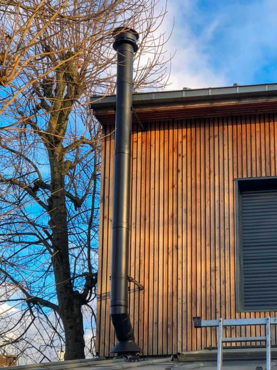 Intérieur chaleureux avec poêle à bois en fonctionnement, flammes visibles à travers la vitre, réserve de bûches intégrée dans la partie basse